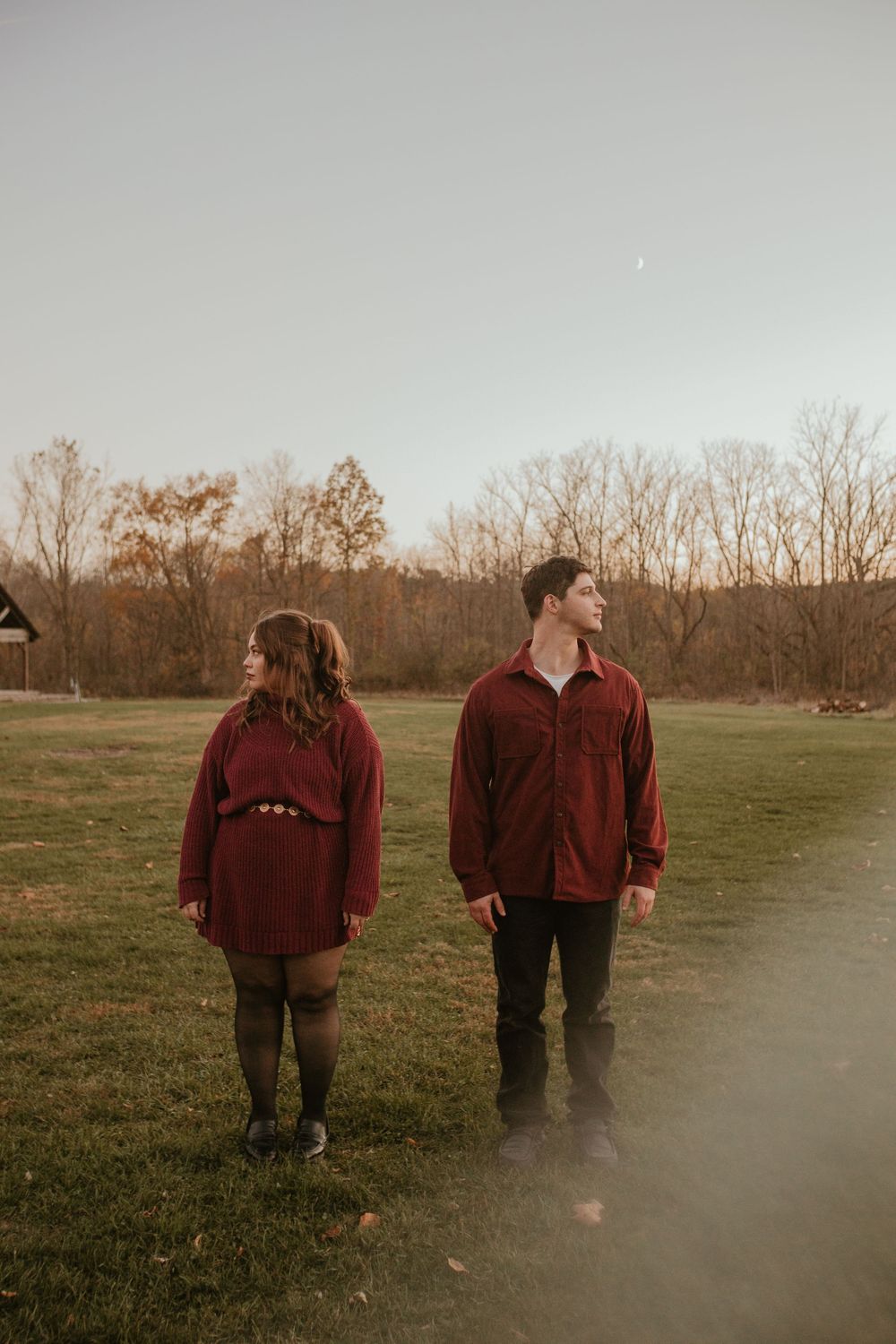 Two people walking together through a misty field at sunset wearing burgundy sweaters.