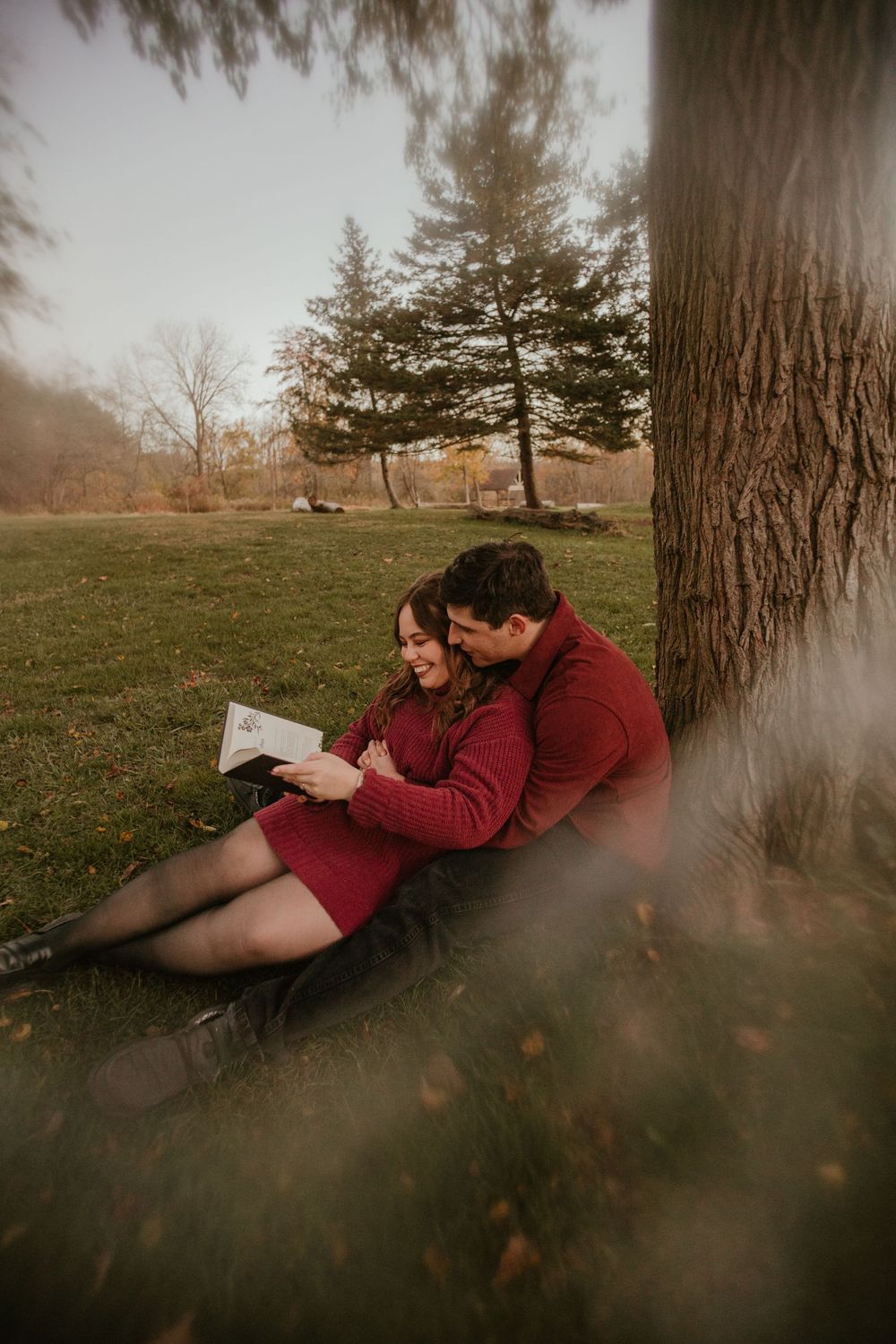 Two people lounging against a tree trunk in a misty field during golden hour.