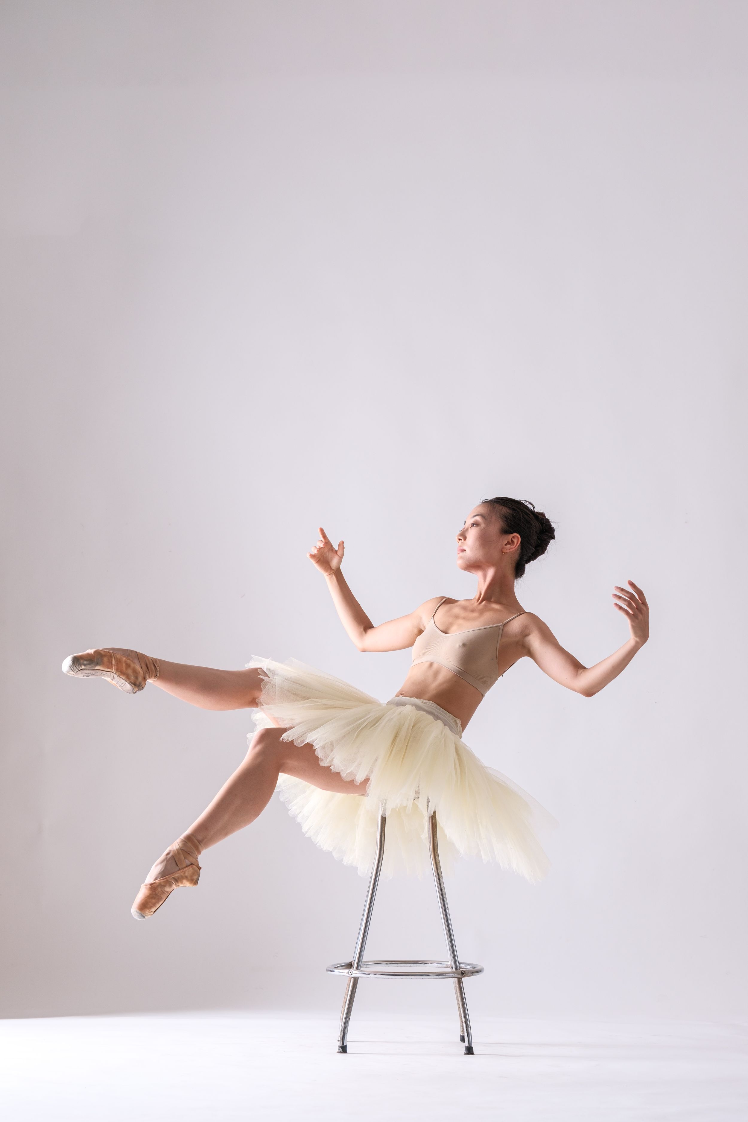 Ballet performer creates dynamic poses while incorporating metal stool in white studio.