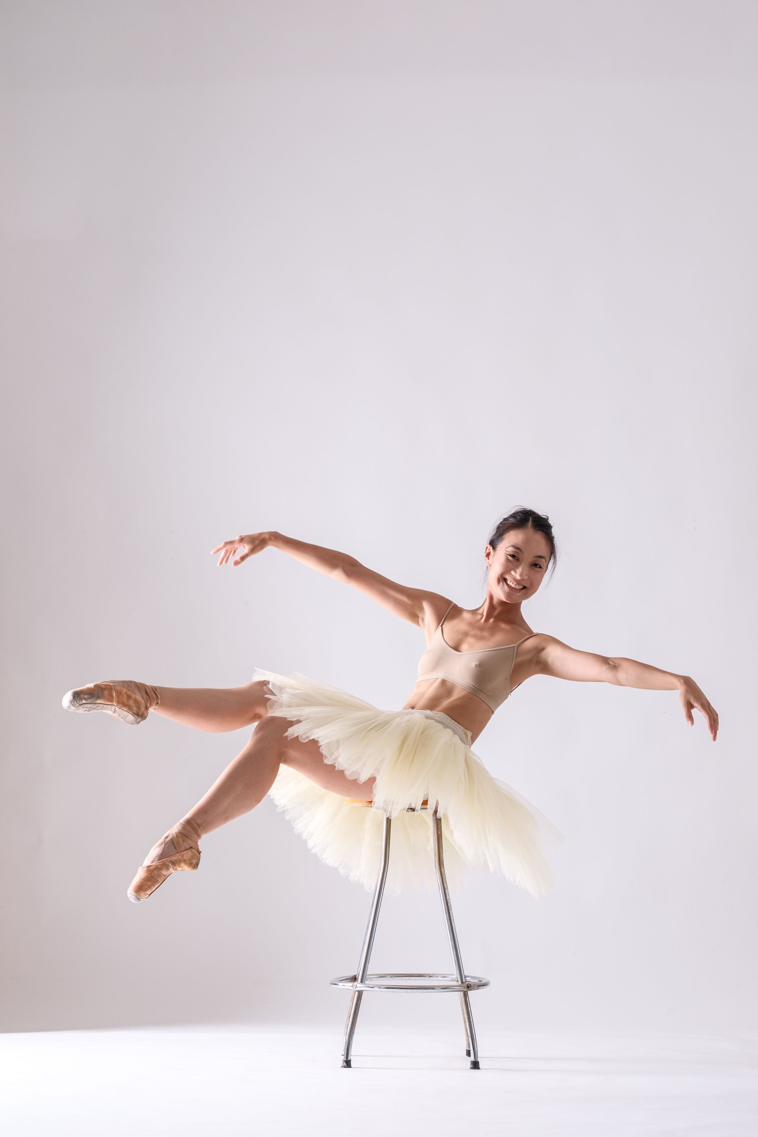 Dancer demonstrates fluid motion sequence using chair prop against stark white backdrop.