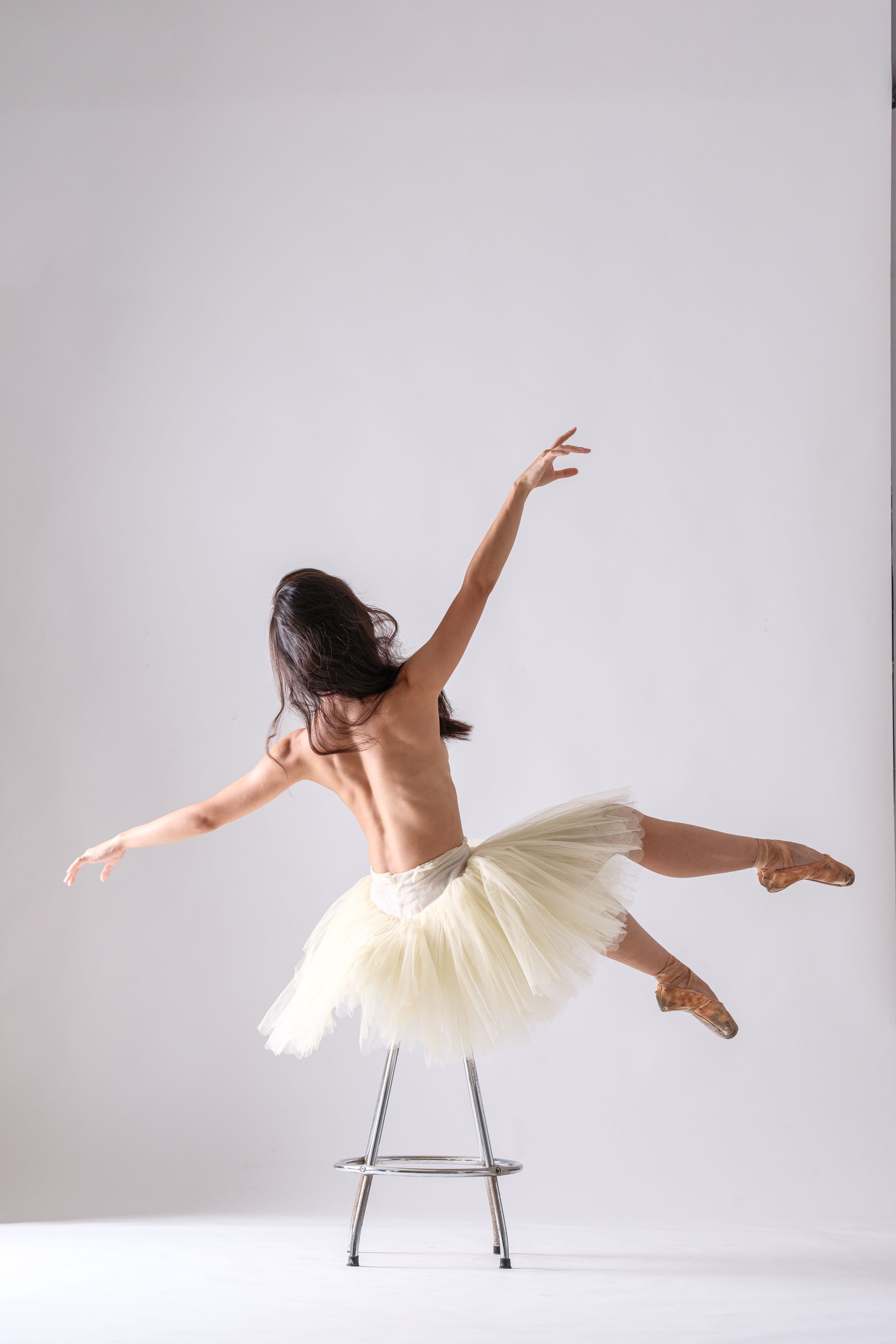 Dancer in pale tulle dress creates flowing movement while using chair as prop in studio.