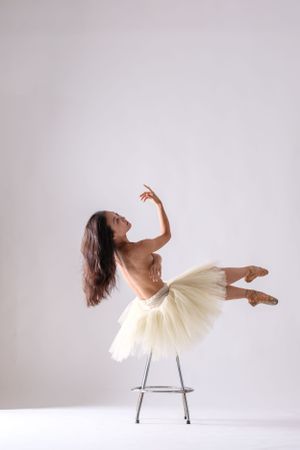 Elegant dance performance captured in profile showing fluid motion with chair prop against white background.