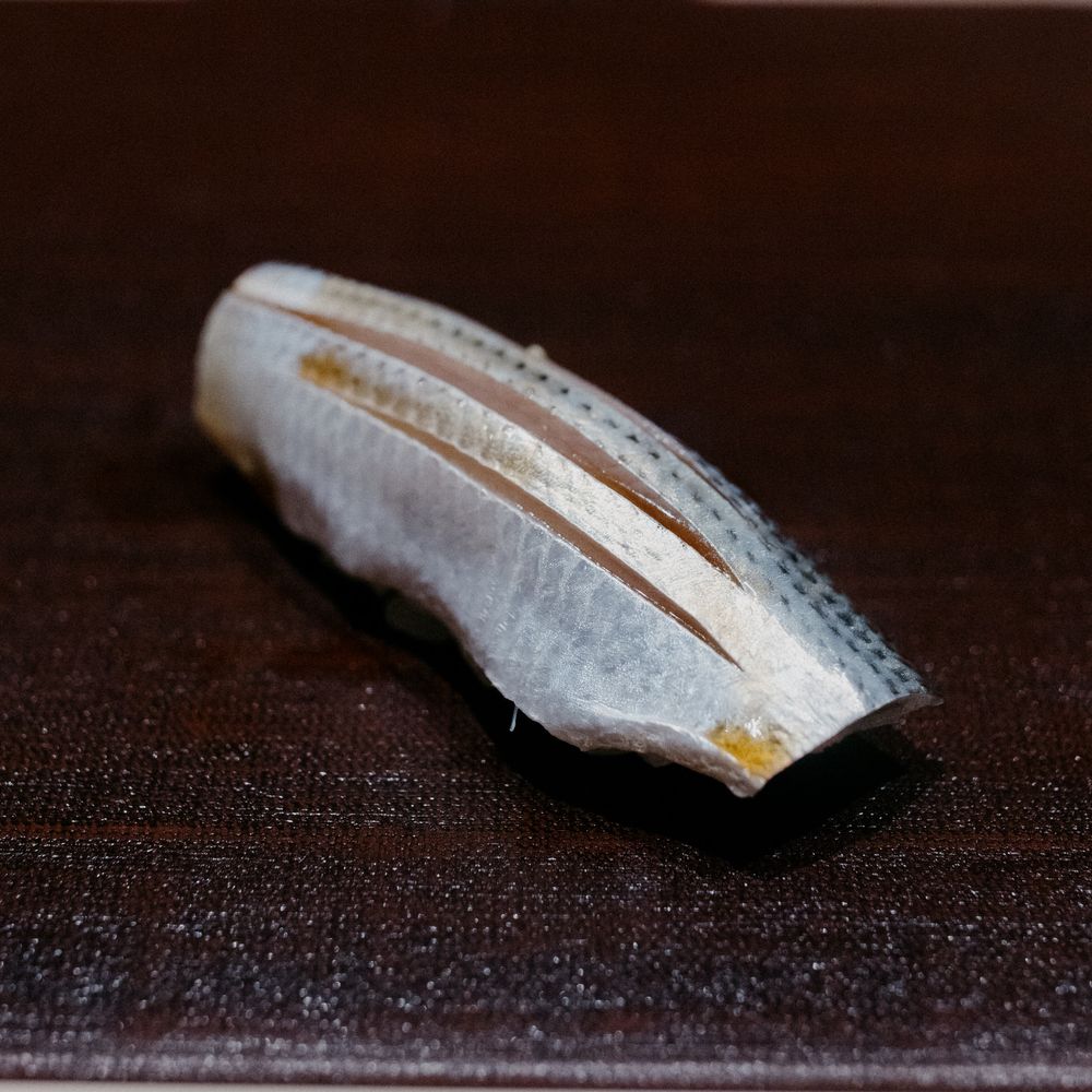 Close-up of a mackerel fillet with silvery skin on a dark surface.