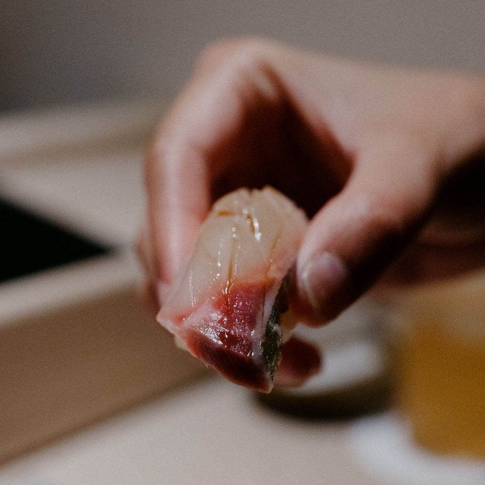 Hand holding a piece of translucent white fish sushi.