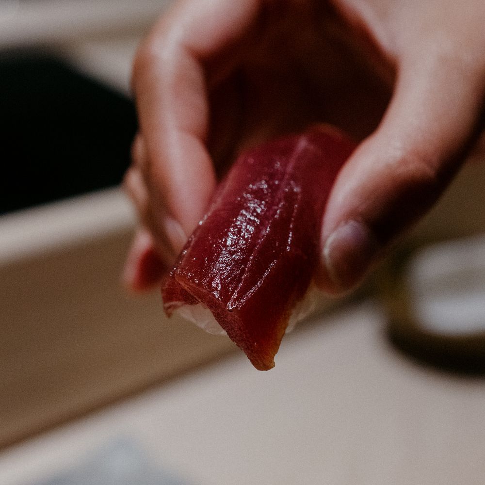 Hand holding a bright red piece of tuna sashimi.