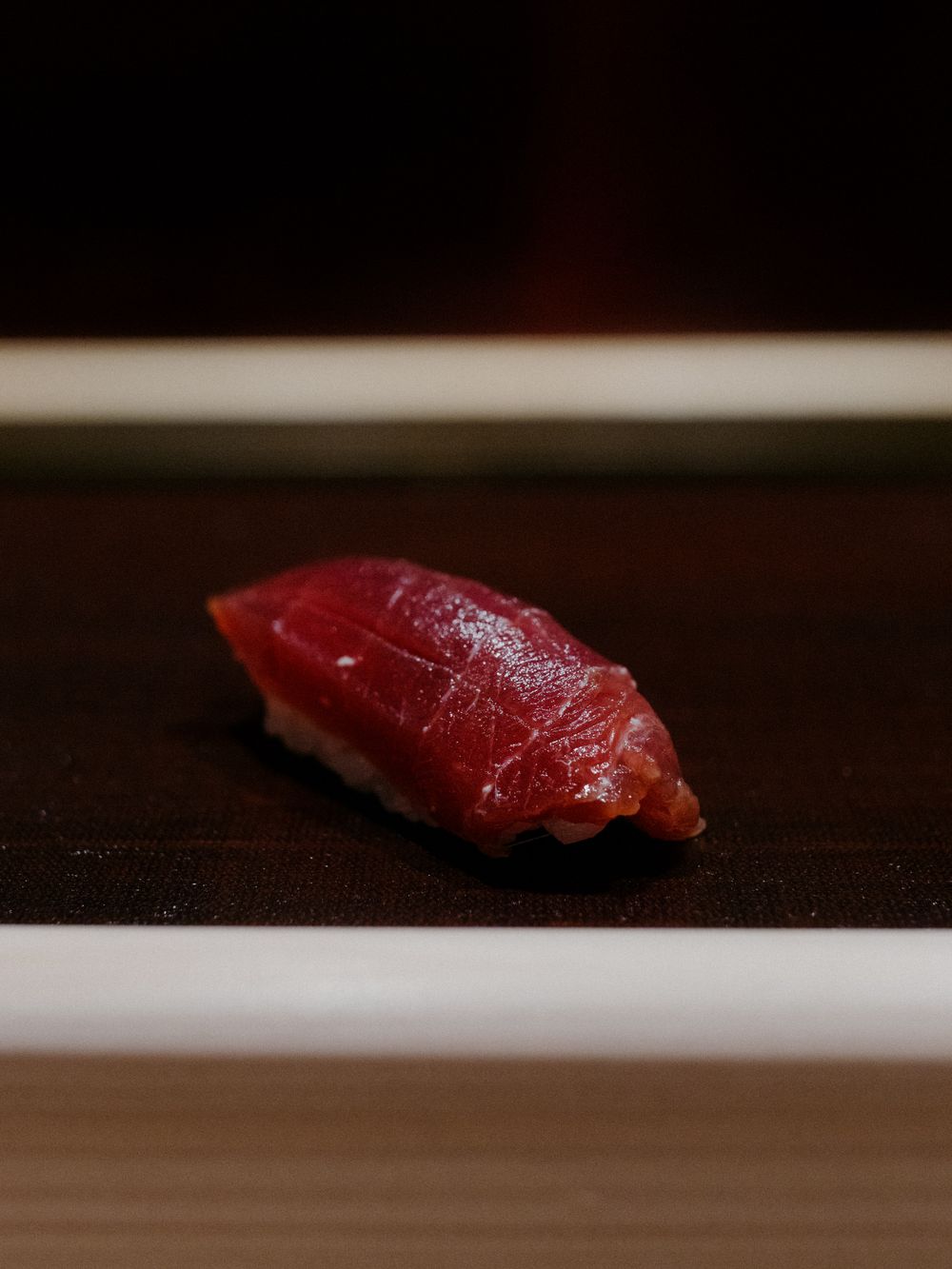 Vibrant red tuna nigiri sushi on a dark surface.