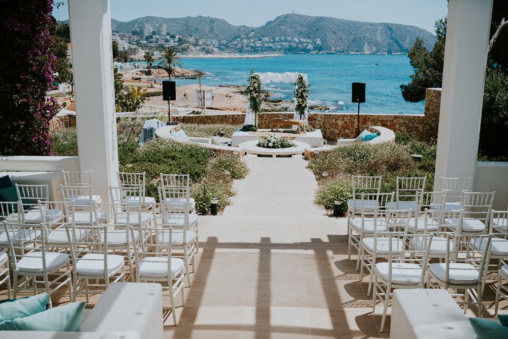 White chairs line a wedding ceremony aisle with stunning coastal views in the background.
