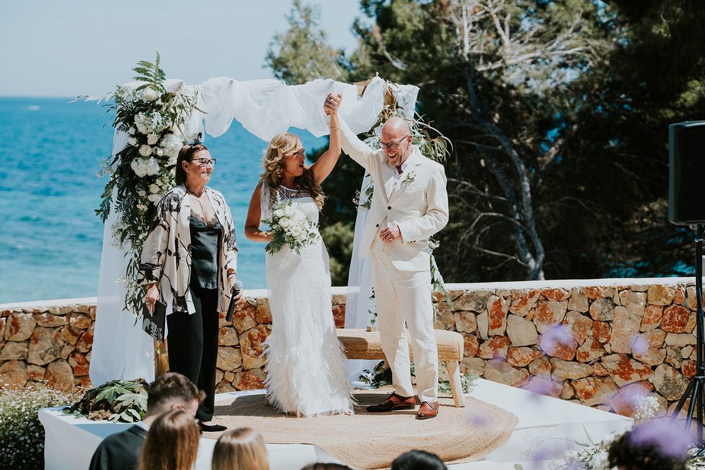 A celebration moment during a seaside wedding ceremony with white draped arch.