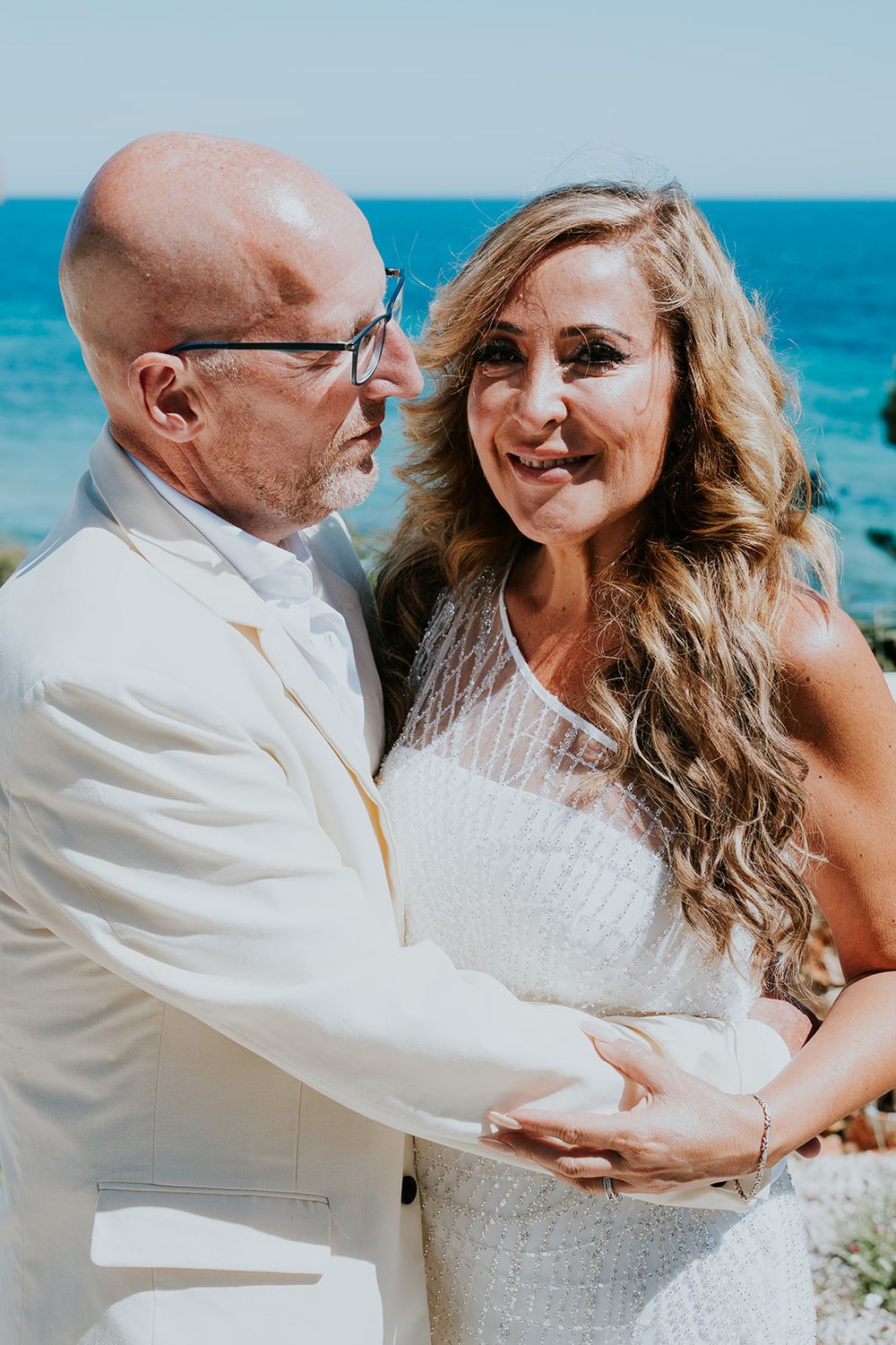 Romantic wedding portrait with turquoise ocean backdrop and stone wall garden setting.