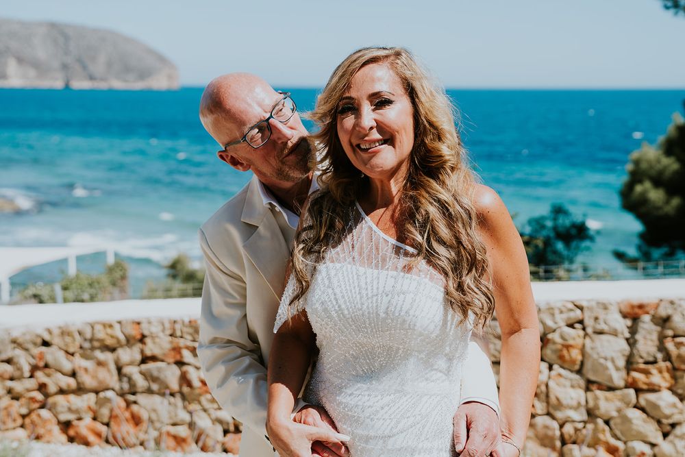 Candid wedding moment captured against beautiful coastal scenery and stone wall.