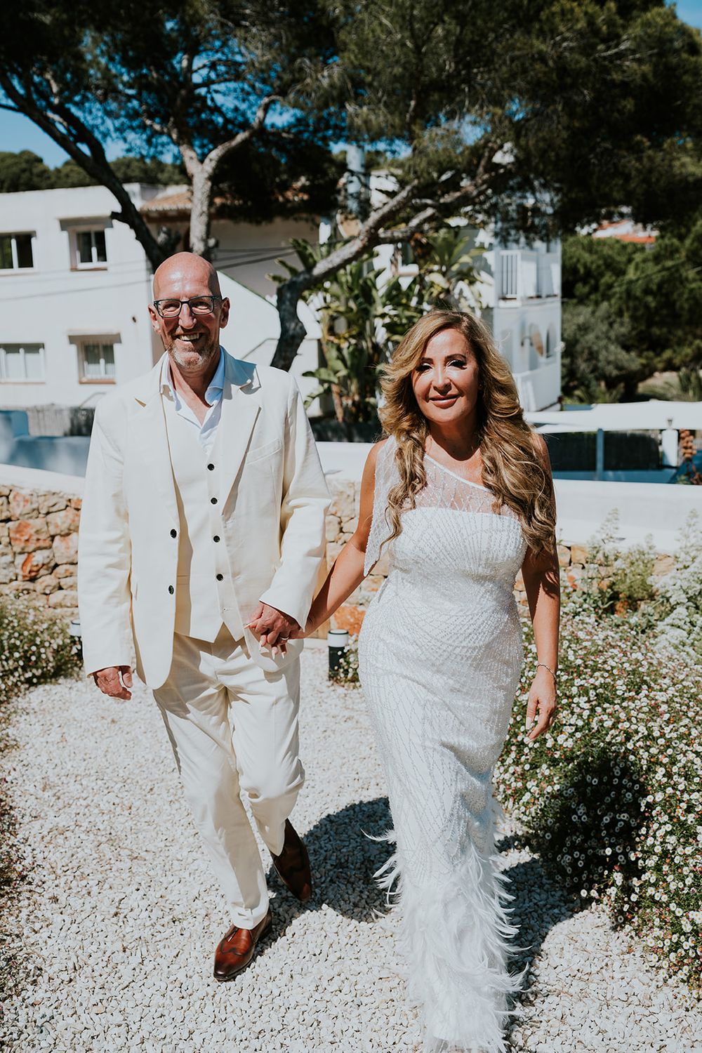 Happy couple walks hand in hand through garden path on their wedding day.