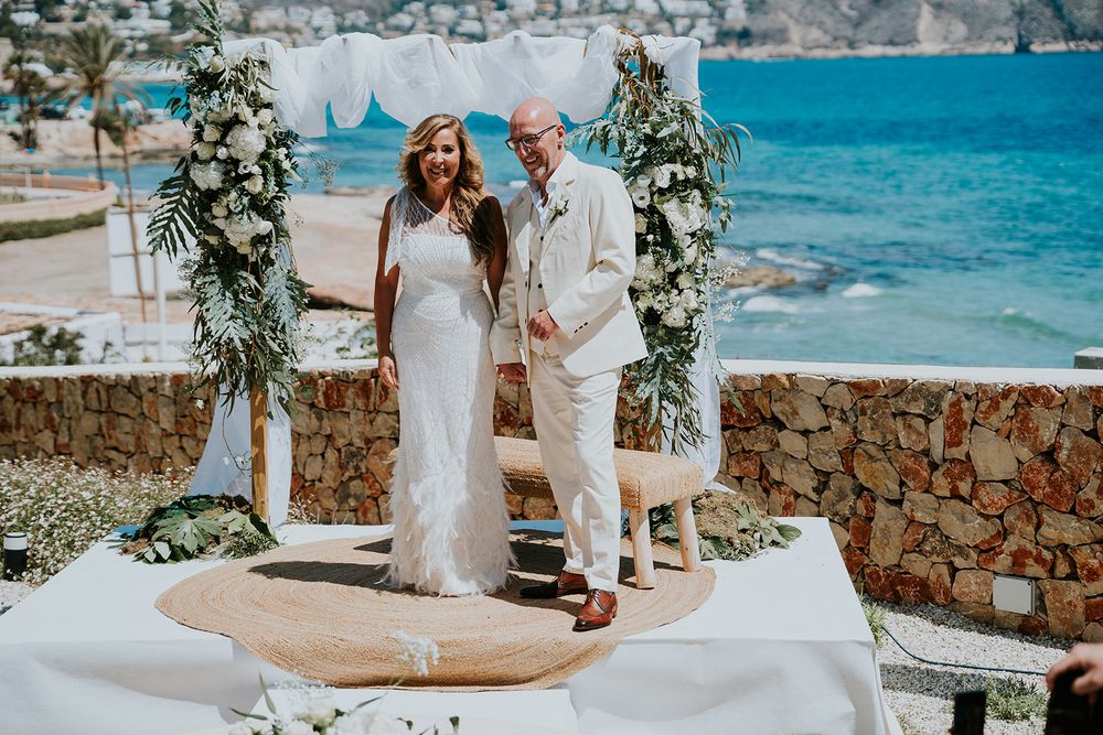 A couple celebrates during their beach wedding ceremony with blue ocean views.