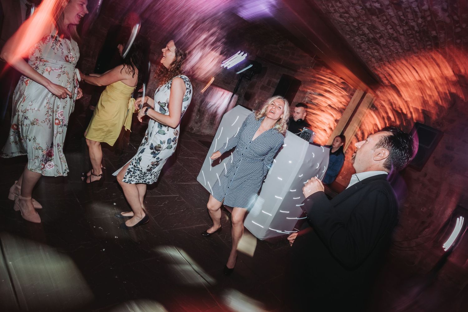 Wedding guests dancing and celebrating on a dimly lit dance floor with motion blur effects.