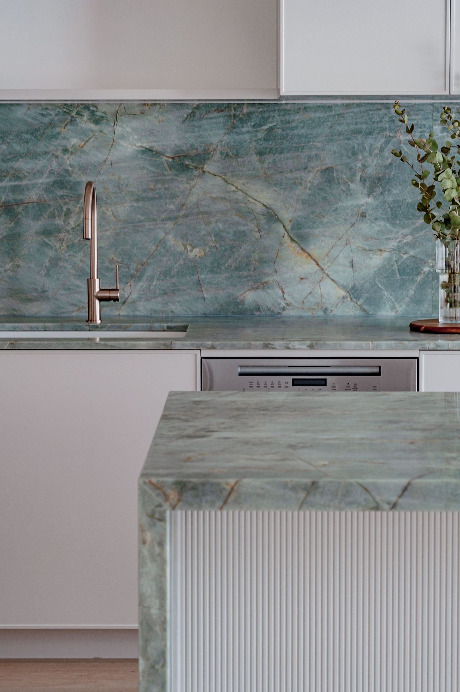 Sleek kitchen counter with sage green marble surfaces and minimalist copper faucet.