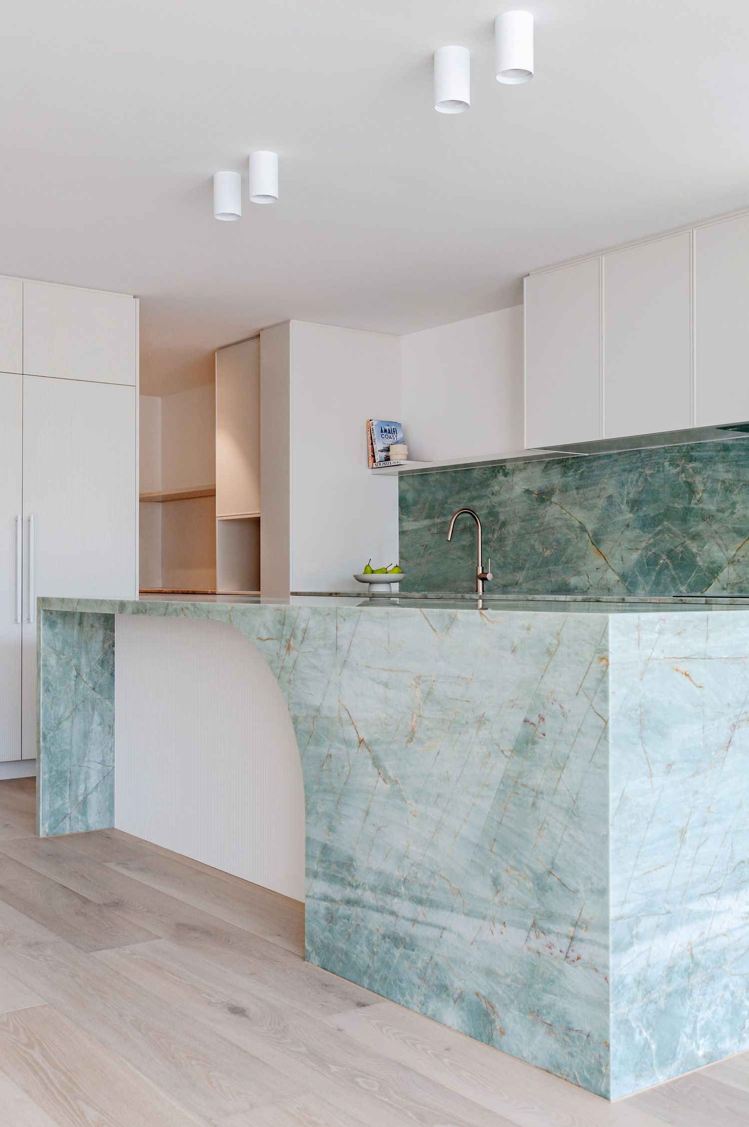Contemporary kitchen featuring curved marble island and matching backsplash in seafoam green.