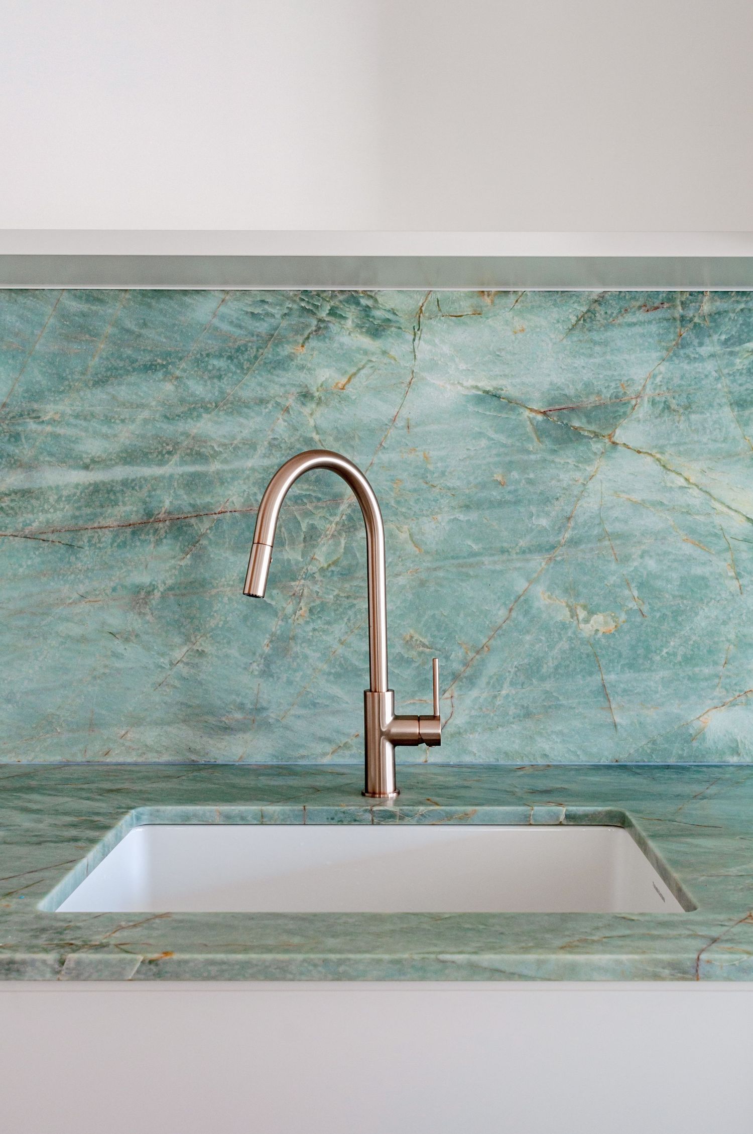 Detail shot of stainless steel faucet against green marble backsplash and countertop.