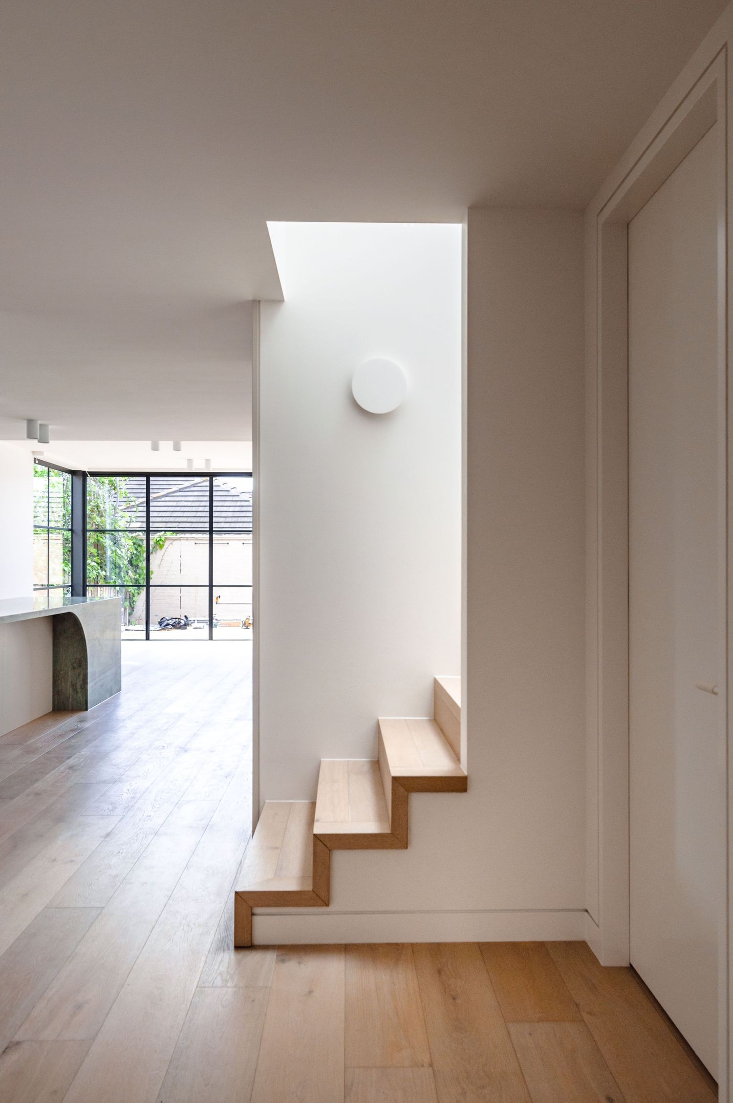 Floating wooden stairs with white walls and natural light from skylight above.
