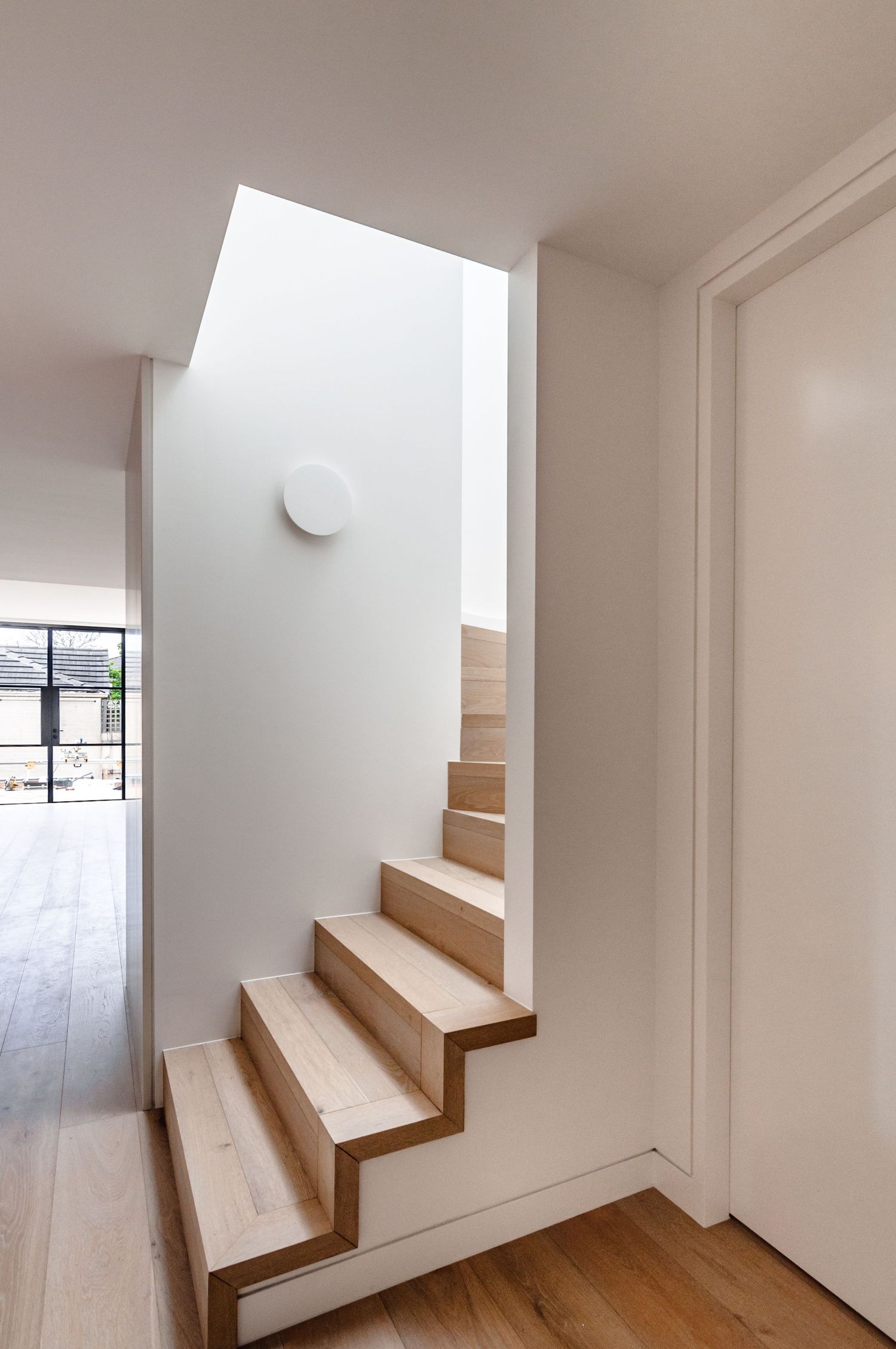 Modern wooden staircase with white walls and minimalist design features natural light from above.