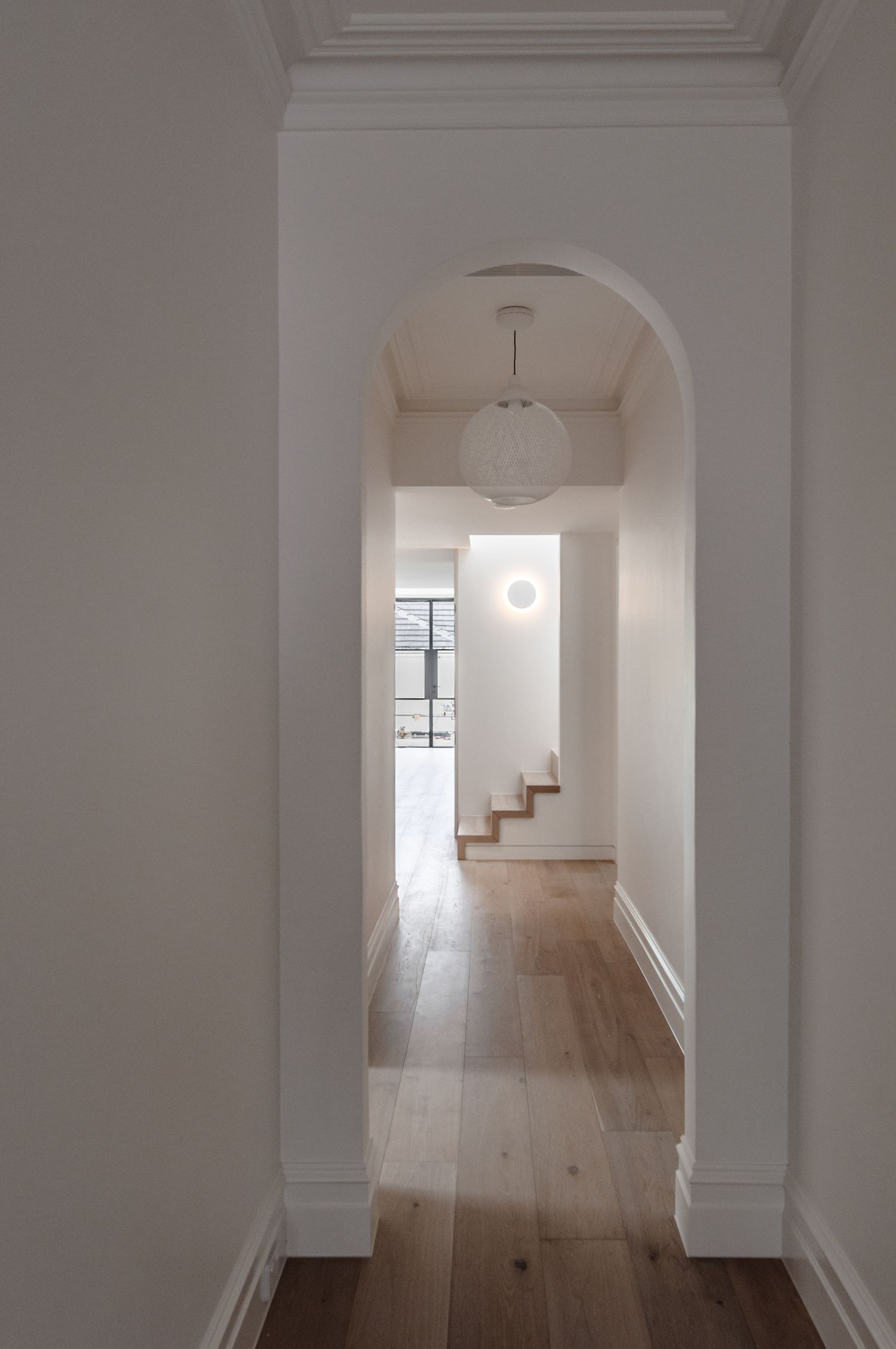Elegant hallway with arched doorway, hardwood floors and pendant lighting leading to a staircase.
