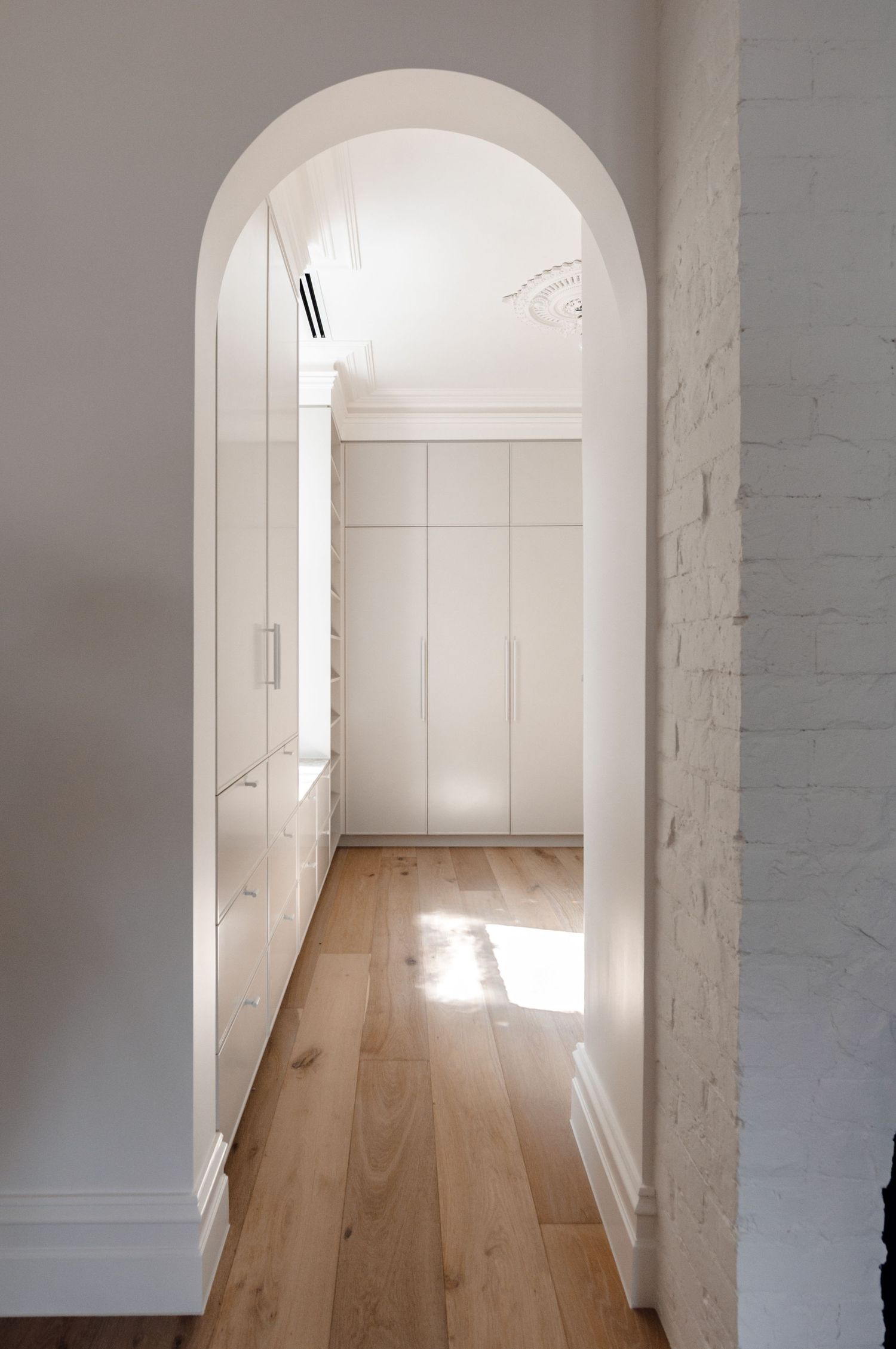 Bright white arched hallway with built-in storage and natural wood flooring.