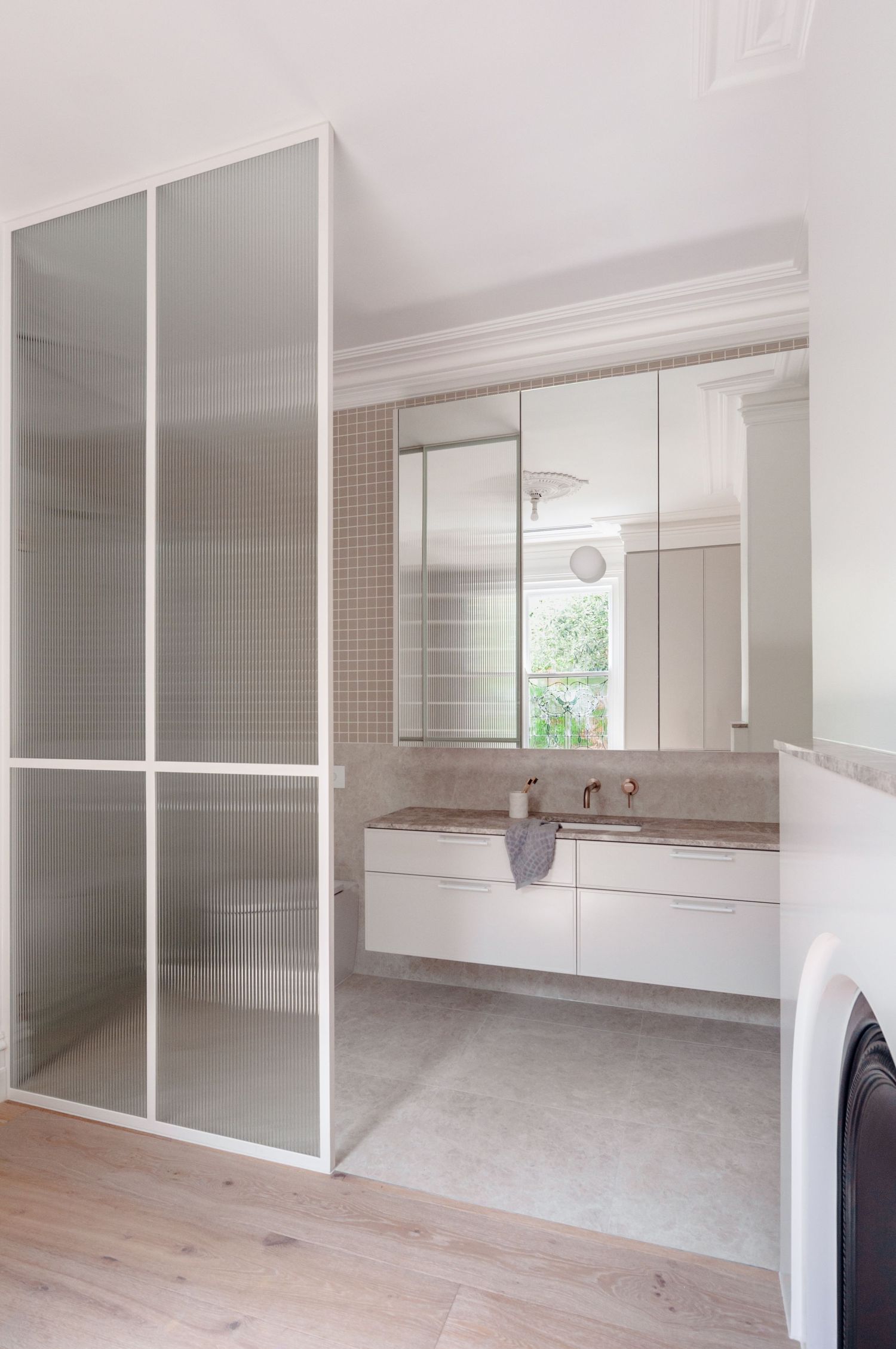 Modern bathroom with frosted glass partition, white vanity, and wood flooring.