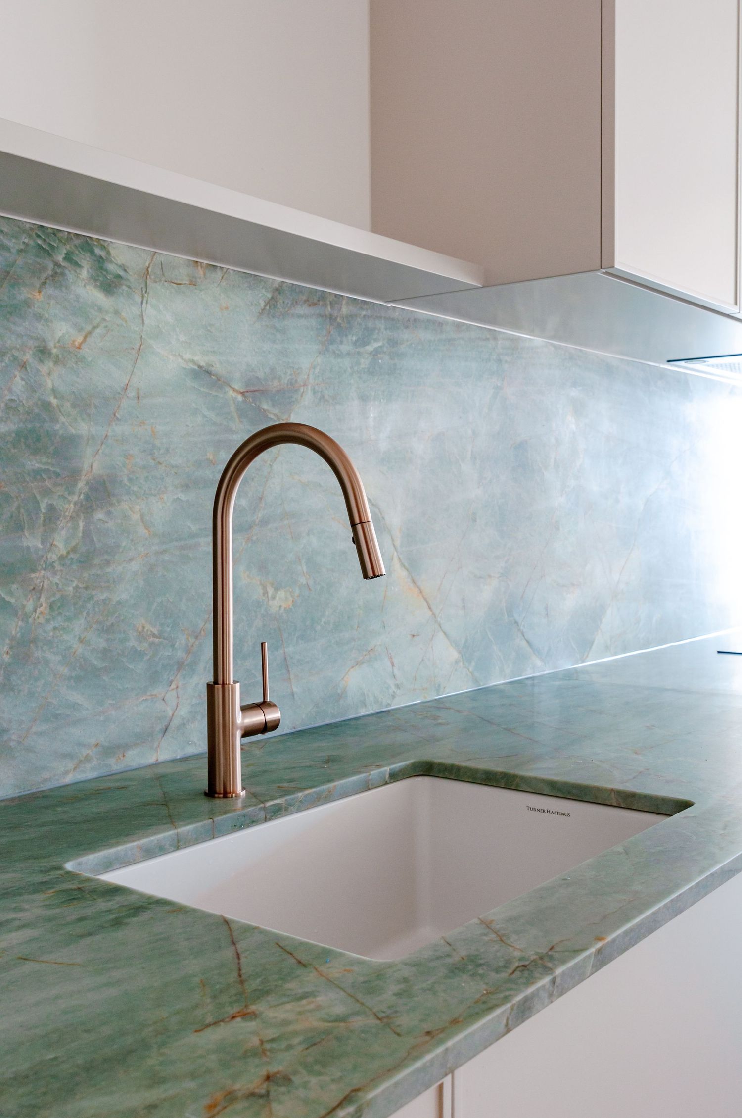 Luxurious kitchen counter with green marble surface and brass faucet against seafoam backsplash.