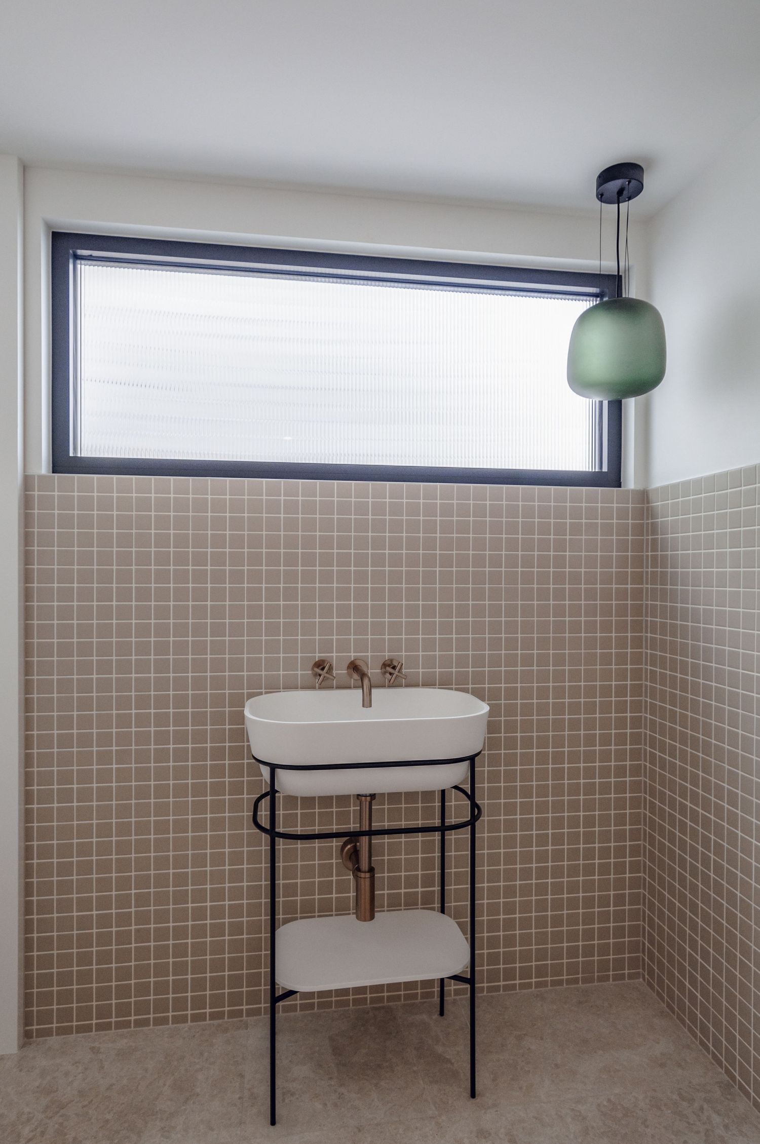 Modern bathroom with beige tile, oval sink on metal stand, and horizontal window.