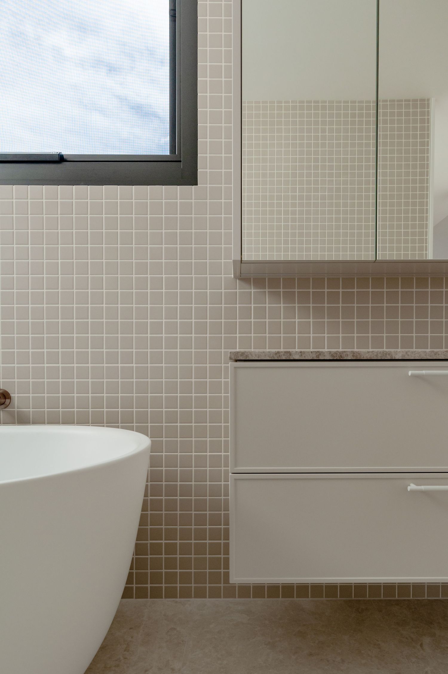 Modern bathroom interior with freestanding tub, wall-mounted vanity and beige tile mosaic wall.