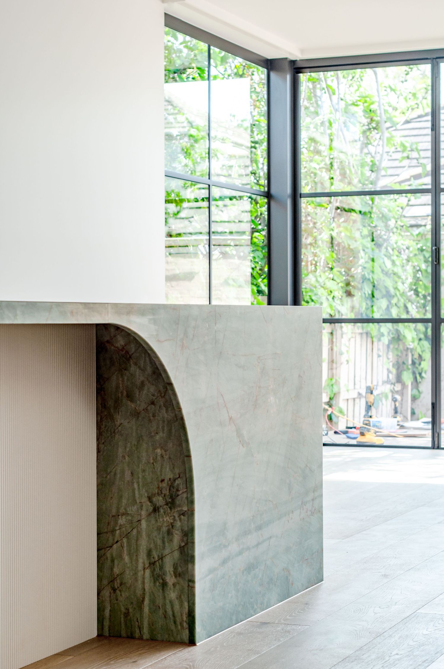 Modern interior featuring a curved marble wall panel and large floor-to-ceiling windows with garden views.