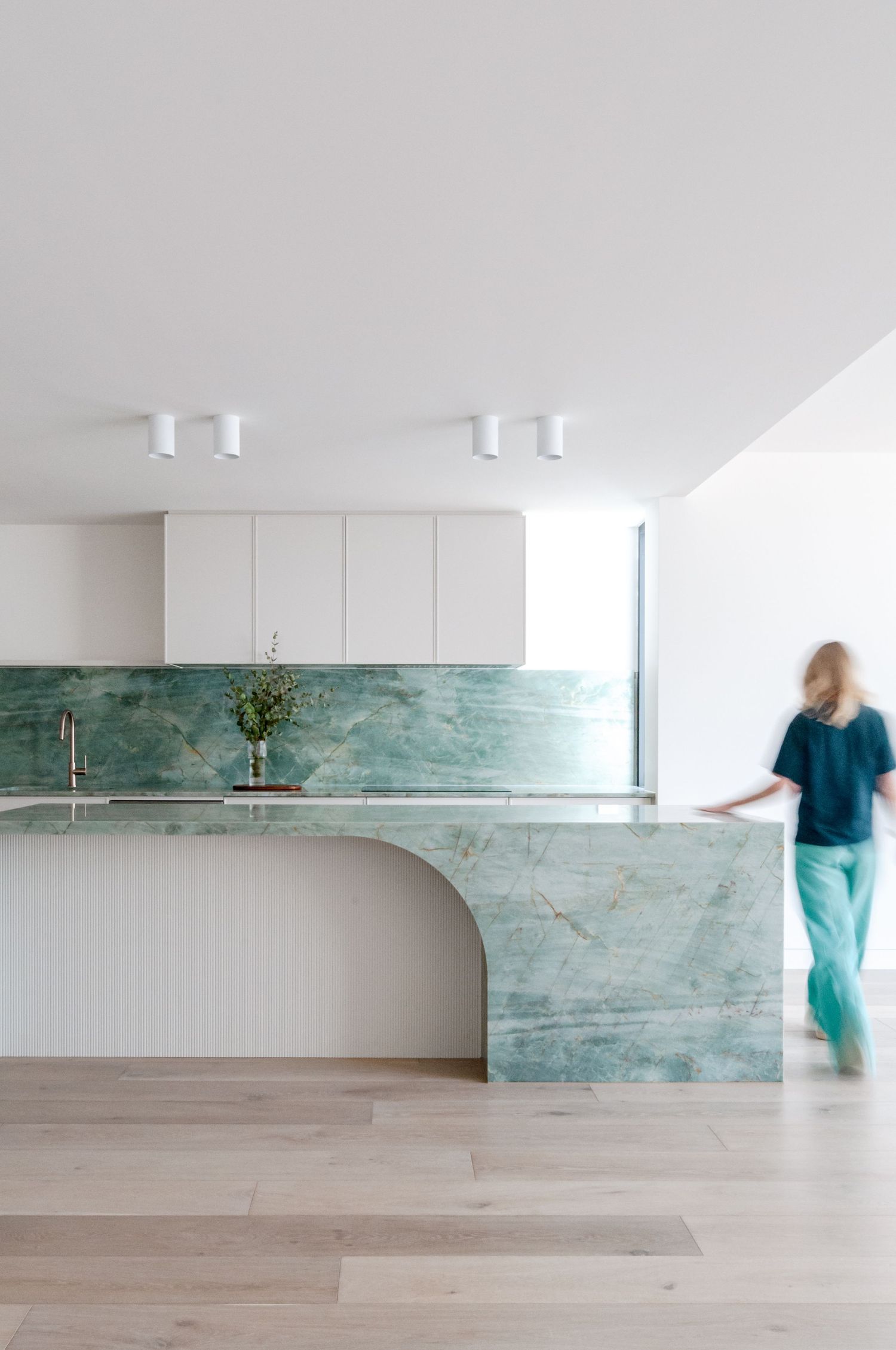Minimalist kitchen with turquoise marble countertops, white cabinets and hardwood flooring.