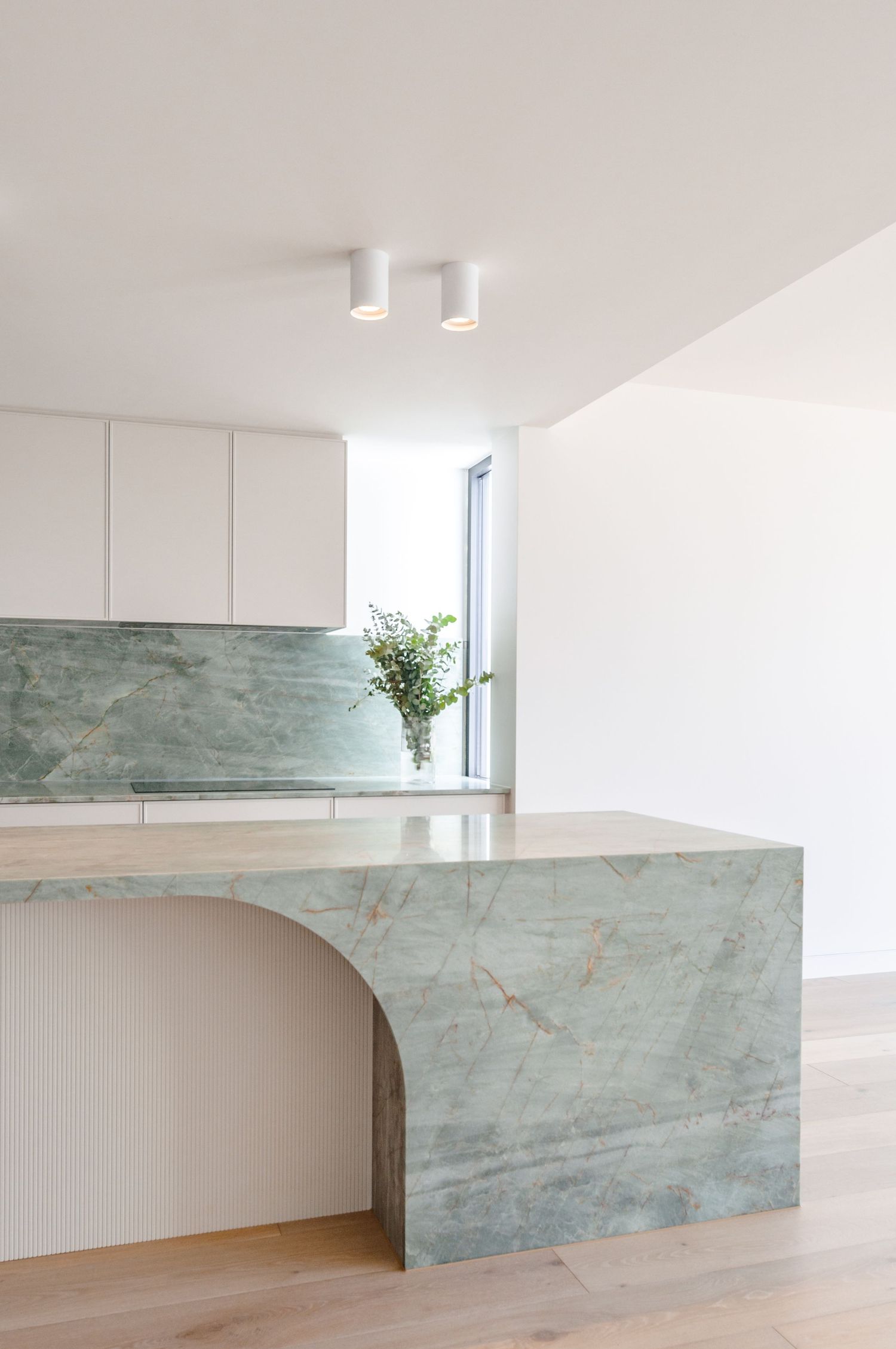 Minimalist kitchen design with curved marble island and seafoam green backsplash.