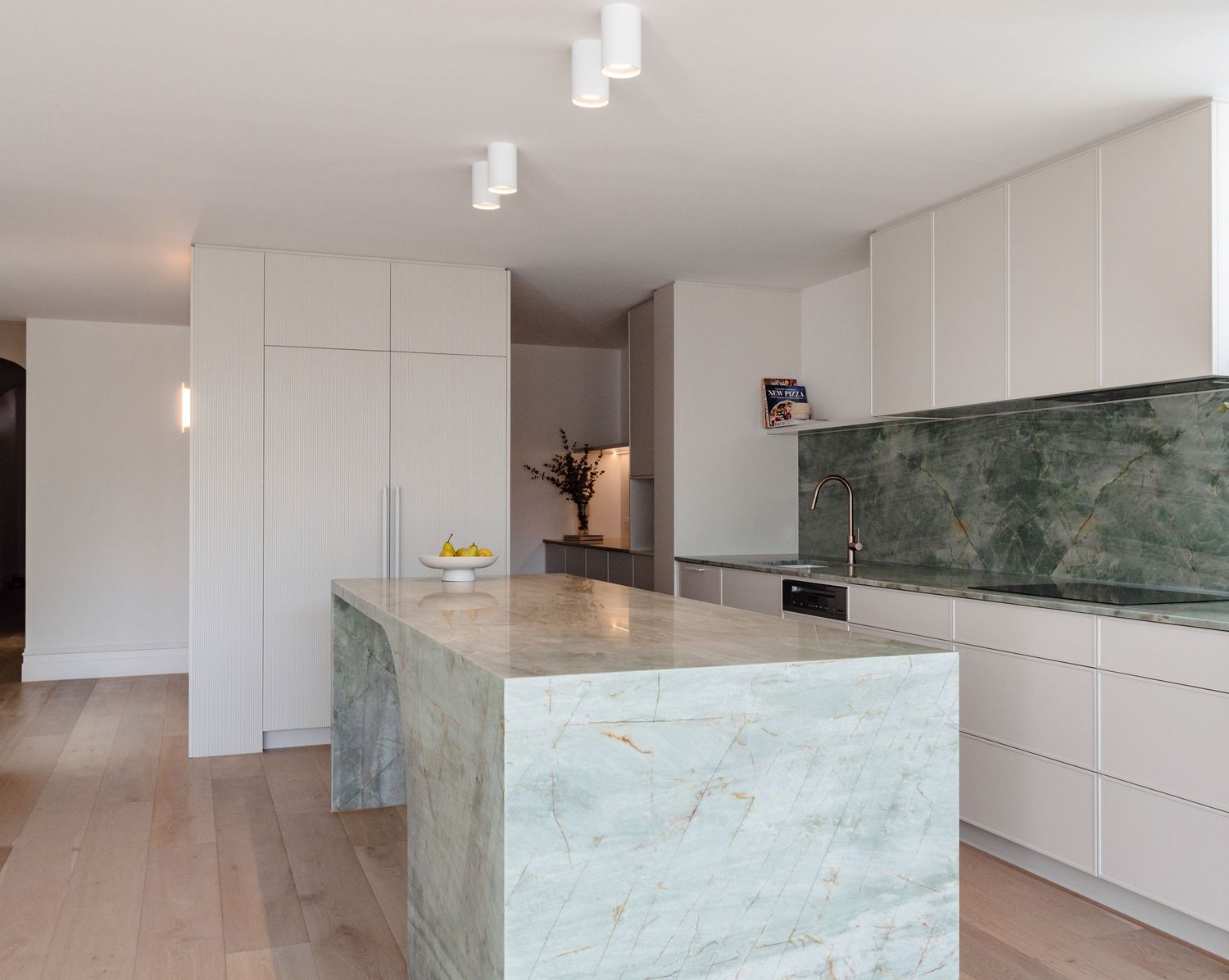 Contemporary kitchen space with dramatic green marble waterfall island and white cabinetry.
