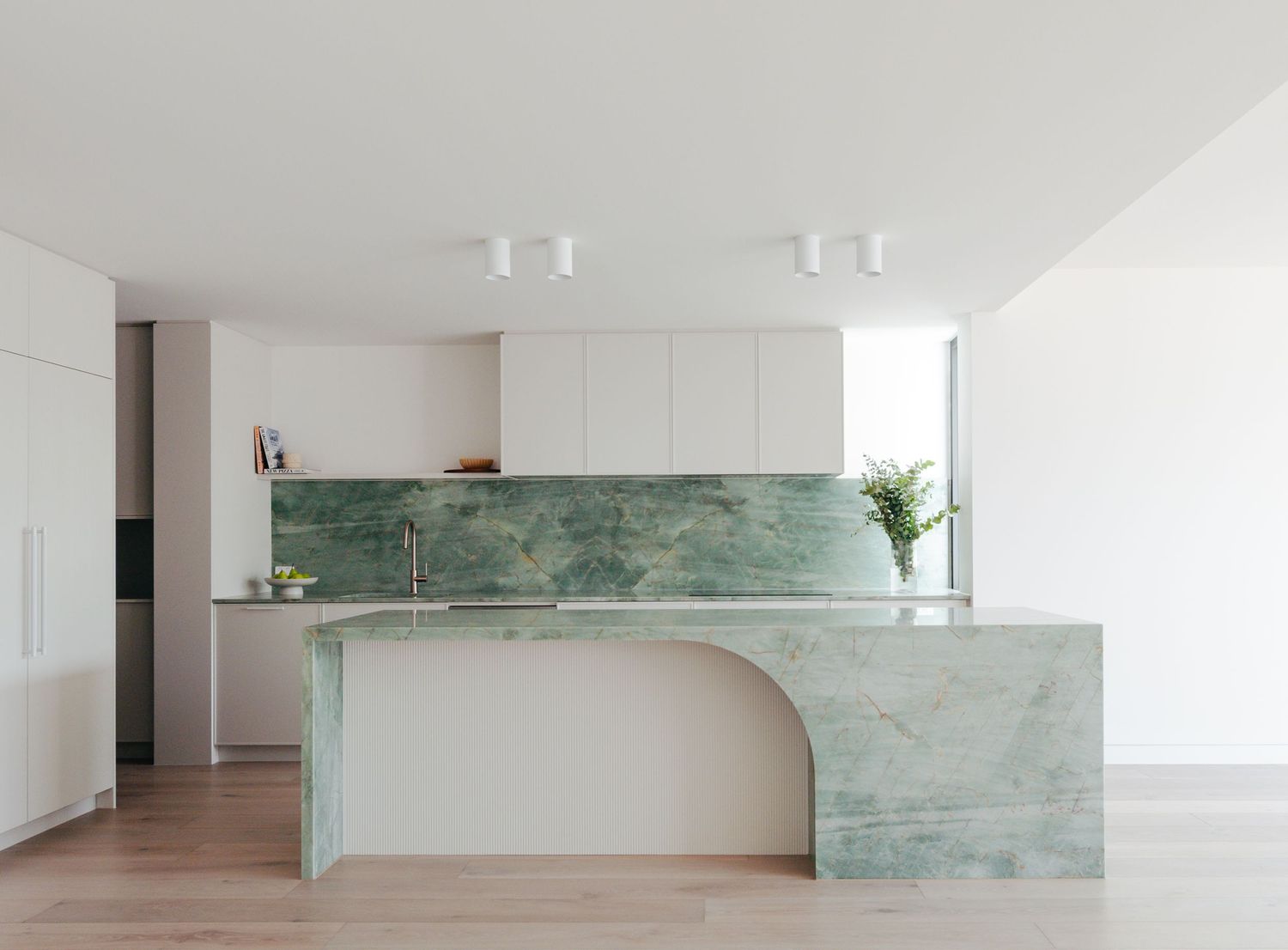 Minimalist white kitchen with striking green marble backsplash and curved island design.