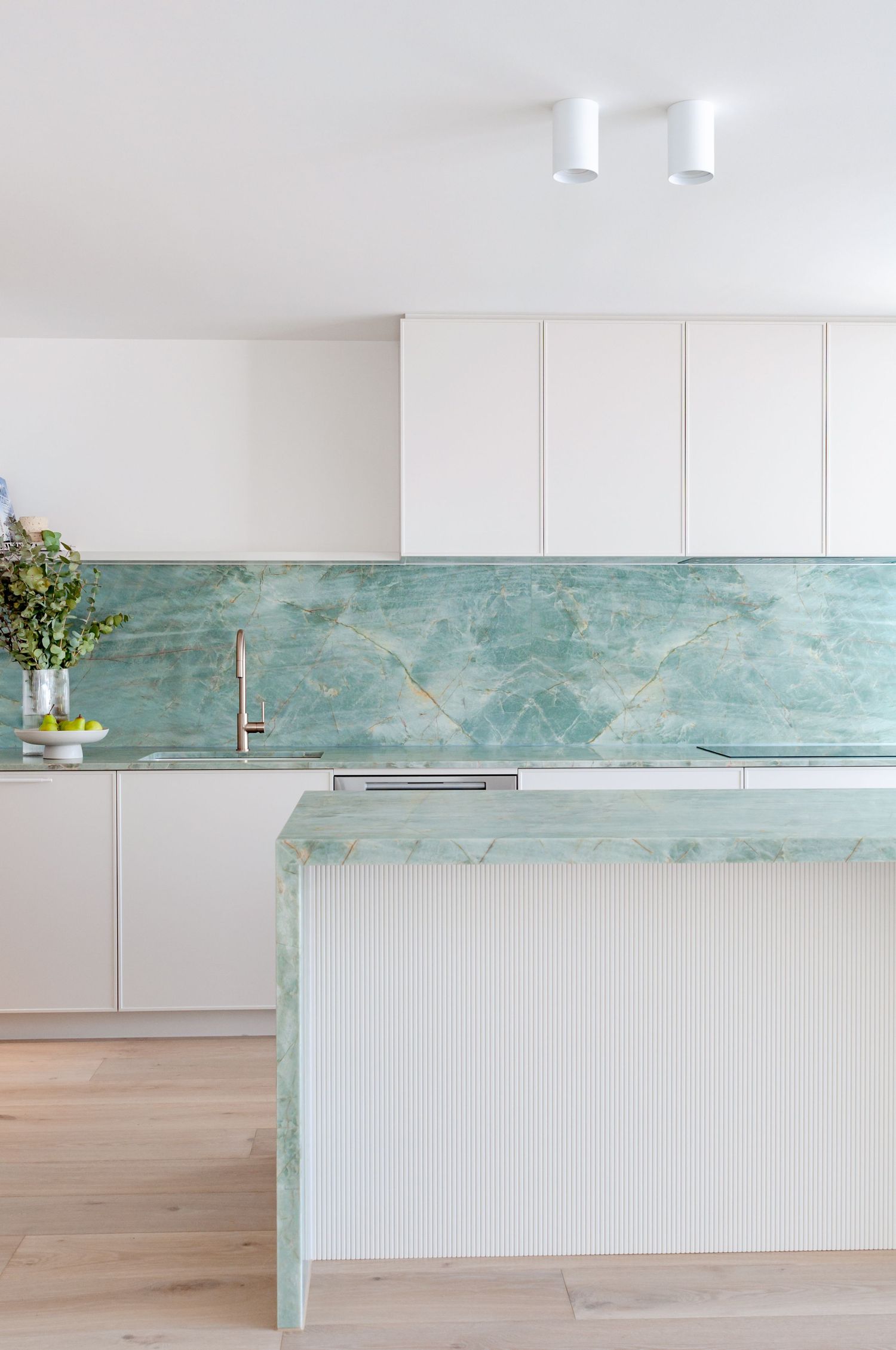 Sleek kitchen design with mint green marble surfaces and white cabinetry against natural wood flooring.