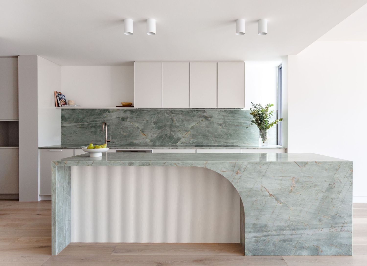 Contemporary kitchen featuring curved marble island and white cabinetry with minimal design.