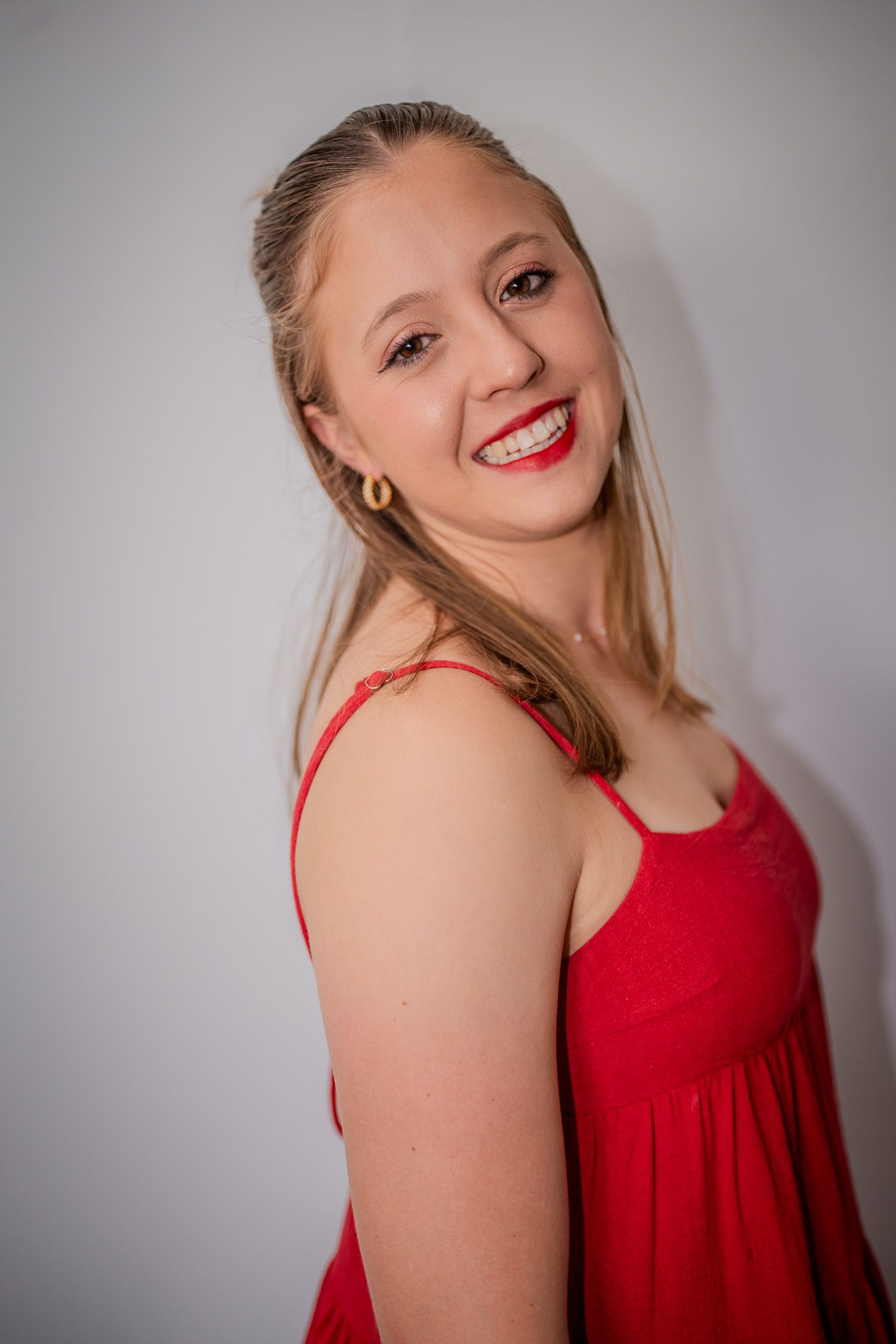 Portrait of someone in a red dress smiling against a gray background.