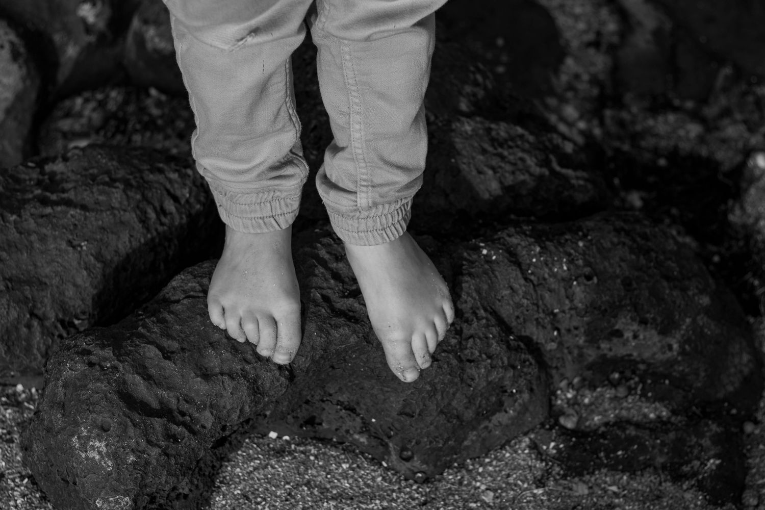 Small bare feet standing on dark rocky surface, captured in black and white.