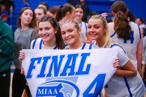 Students hold up MIAA Final Four sign while celebrating at basketball game.