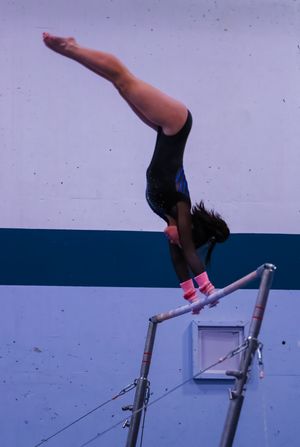 Gymnast executing an inverted move on uneven bars with precise form.