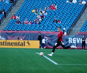 Empty blue stadium seats provide backdrop for soccer match on green turf field.