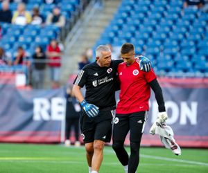 Athletes stretch and prepare on soccer field before match with stadium seating visible.
