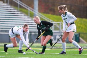 Field hockey athletes dive and lunge for the ball during intense ground play.