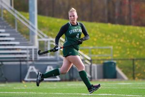 Field hockey players in green uniforms compete for ball control on artificial turf.