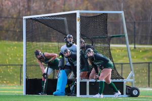 Field hockey goalie defends the net while teammates protect against opposing attack.