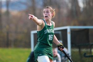 Field hockey athletes in green uniforms position themselves during competitive play.