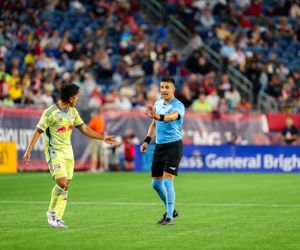 Professional soccer match shows players competing in yellow and blue uniforms on grass field.
