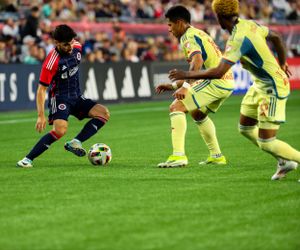 Soccer players scramble for ball control during competitive match on pristine grass field.