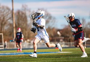 Multiple lacrosse players compete for ground ball possession on a grass field.