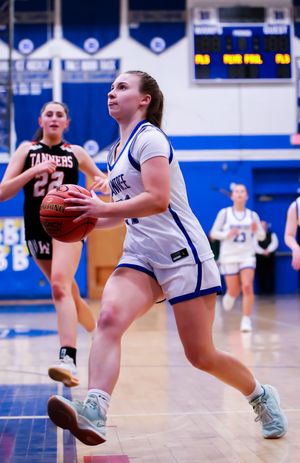 Basketball player in white jersey drives toward the basket during high school game in blue gymnasium.