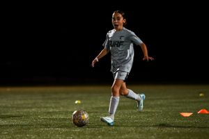 Soccer player dribbles ball during practice drill on outdoor field at dusk.